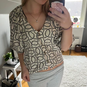 Mönstrad blus - Säljer en beige blus från H&M med svarta prickiga mönster i cirklar. Blusen har v-ringning, knappar framtill och trekvartsärmar med lätt puff. Perfekt för dig som gillar unika mönster och en avslappnad men snygg stil. Hör av dig vid frågor🥰