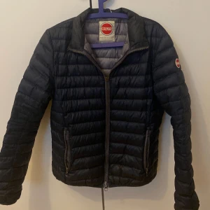 Svart Colmar pufferjacka - Säljer en svart pufferjacka från Colmar med klassisk quiltad design och dragkedja framtill. Jackan har lång ärm, två fickor med dragkedja och rundad krage. Perfekt för kyliga dagar och enkel att matcha med olika outfits.