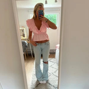 Ljusrosa volangblus  - Supersöt ljusrosa blus med djup v-ringning och volangdetaljer längs halsen och axlarna. Modellen är croppad och har korta ärmar med extra volym. Perfekt för dig som gillar romantisk och trendig stil.