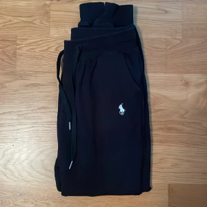 Svarta mjukisbyxor från Polo Ralph Lauren - Svarta mjukisbyxor från Polo Ralph Lauren med klassisk vit logga broderad på benet.  Perfekta för chillkvällar eller gymet. Tillverkade i mjukt bomullsmaterial för extra komfort. Använda knappt ligger bara och skräpar i garderoben inga tecken på användning. Kan sänka vid snabb affär. 