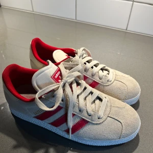 Röd/beiga gazelle adidas skor - Säljer dessa superfina adidas gazelle skor i storlek 38, de är i fint skick endast använda några gånger men syns knappt på utsidan! 