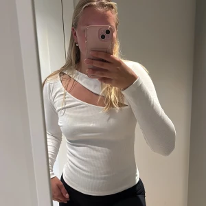 Vit ribbad topp med cut out NLY Trend - Trendig vit långärmad topp från NLY Trend i ribbad bomullskvalitet. Snygg cut out-detalj vid axeln som ger en cool och modern look. Perfekt att styla med jeans eller kjol för en stilren outfit.