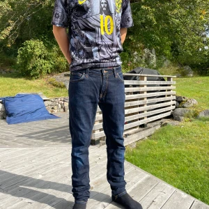 Mörkblå jeans från Nudie Jeans - Säljer ett par mörkblå jeans från Nudie Jeans med klassiska orange sömmar och snygga detaljer på bakfickorna. Jeansen har normal passform och raka ben, tillverkade i slitstark bomull. Perfekta för dig som gillar stilrena och tidlösa jeans. Jeansen är i w32 l32, modellen skinny len!