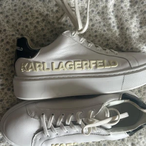 Vita sneakers från Karl Lagerfeld - Snygga vita sneakers från Karl Lagerfeld med tydlig logga i 3D på sidan och svart glansig detalj på hälen. Använda Max tre gånger, de är som nya!! Pris kan diskuteras!