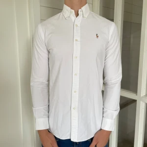 Polo Ralph lauren skjorta - Säljer denna riktigt snygga vita Ralph lauren skjorta! Den är i mycket bra skick utan några defekter, storlek S modell slim fit, den är 75 cm lång och 46 cm bred under armhålorna, jag på bilden är 184 cm och väger 82 kg, hör gärna av dig vid frågor!
