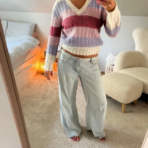 Randig stickad tröja med glitter - Köpt i Köpenhamn! Superfin stickad tröja med breda ränder i vitt, lila, rosa och vinrött. Tröjan har v-ringning, lång ärm och croppad passform. Perfekt för dig som gillar en mysig och färgglad look. Materialet är mjukt och luftigt stickat.