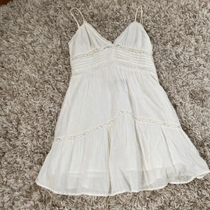 Vit sommarklänning från Zara XS - Supersöt vit klänning från Zara i storlek XS. Den har tunna axelband, v-ringad hals och fina spetsdetaljer längs midjan och kjolen. Klänningen är kort och har en flowy passform med volangkant nedtill, perfekt för varma dagar. Materialet är mjukt och lätt linne. Den köptes i Nice, Frankrike sommaren 2024 men är nu för liten.