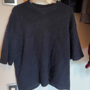 Mörkblå stickad tröja med halvärm från Gina tricot  - Mysig mörkblå stickad tröja med halvärmar. Tröjan har en enkel och stilren design, perfekt att matcha med jeans eller kjol. Den stickade strukturen ger en skön känsla och passar bra när det är lite kyligare ute. Endast använd en gång