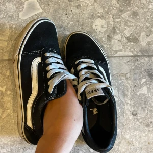 Svarta Vans sneakers strl 38 - Klassiska Vans Old Skool sneakers i svart med vit sula och vit sidostrip. Skorna har snörning och rund tå, tillverkade i canvas och mocka. Använda men ändå fina enligt mig! 