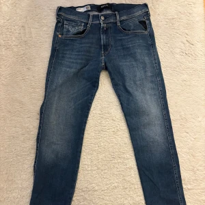 Replay Anbass blå jeans herr - Säljer ett par snygga Replay Anbass jeans i klassisk blå tvätt. Modellen är slim fit med smal passform och raka ben. Jeansen har fem fickor, dragkedjegylf och diskreta slitningar för en cool look. Materialet är mjukt och stretchigt för extra komfort.