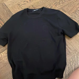Svart ribbad t-shirt Gina Tricot XS - Svart t-shirt från Gina Tricot i storlek XS. Modellen har korta ärmar och ribbade muddar vid ärmslut och hals. Materialet känns mjukt och stretchigt, perfekt för en chill och enkel look. Passformen är normal och färgen är helsvart.