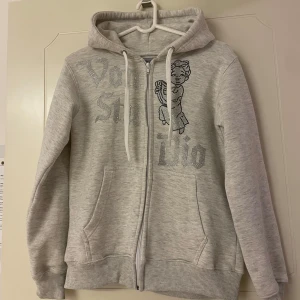 Ljusgrå hoodie med strass från Vonstudio - Säljer en ljusgrå hoodie från Vonstudio i storlek XS. Tröjan har huva, dragkedja och fickor framtill. På bröstet finns strassdetaljer med text och en söt ängel. Perfekt för dig som gillar comfy och snygg streetstyle. Tveka inte att höra av er vid minsta fundering! Pris kan diskuteras