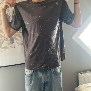 Svart t-shirt med gröna stänk från H&M - Svart t-shirt från H&M med coolt grönt stänkmönster över hela plagget. Klassisk rund hals och korta ärmar. Tillverkad i mjuk bomull som är skön mot huden. Perfekt för dig som gillar streetstyle och vill sticka ut lite extra.