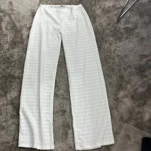 Vita vida byxor med strukturmönster - Säljer ett par vita byxor med breda, raka ben och ett diskret rutigt strukturmönster i tyget. Byxorna har en luftig och relaxed passform, perfekta för en chill och stilren look. Materialet känns lätt och passar bra till varmare dagar.