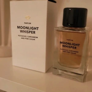 Moonlight Whisper Parfum 50ml - Moonlight Whisper Parfum med doft av pistage, kardemumma och pink sugar. Flaskan är rektangulär i transparent glas med svart lock, och kommer i en stilren vit kartong. Perfekt för dig som gillar unika och söta doftnoter.