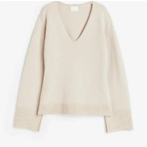 Beige stickad v-ringad tröja - Snygg beige stickad tröja med v-ringad hals och långa ärmar. Tröjan har breda ribbade muddar vid ärmslut och nederkant, vilket ger en cool och avslappnad vibe. Perfekt att matcha med jeans eller kjol för en enkel men stilren look.