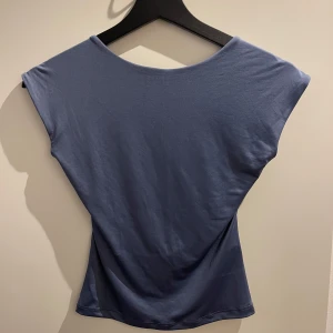 Blå topp med öppen rygg - Snygg blå topp med en stilren design och öppen rygg. Perfekt för en avslappnad och trendig look. Toppen har en enkel och elegant stil som passar till många olika tillfällen.