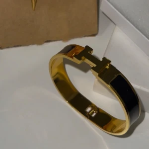 Guldfärgad armband med svarta detaljer - Helt oanvänd och ny. Materialet är rostfritt stål med 18K guldplätering. 