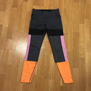 Färgglada leggings från H&M Sport - Snygga och bekväma leggings från H&M Sport i en mix av färger: grå, svart, lila och orange. Perfekta för träning med en tight passform och elastiskt material för maximal rörelsefrihet.