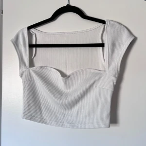 Vit ribbad topp från Shein - Säljer en stilren vit ribbad topp från Shein. Toppen har en croppad design med korta ärmar och en söt hjärtformad urringning. Perfekt för en trendig look! 🌟 Passar mig bra som normalt har S! Önskar du veta exakta mått? Tveka inte att höra av dig!