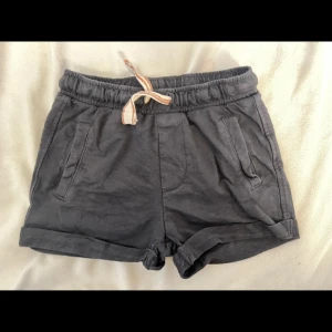Mörkgrå shorts från Newbie - Säljer ett par mörkgrå shorts från Newbie med elastisk midja och snörning. Shortsen har två fickor fram och två bak, samt uppvikta benslut för en avslappnad look. Perfekta för varma dagar!