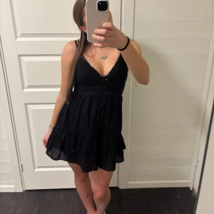 Svart kortklänning med volangdetaljer - Snygg svart kortklänning med volangdetaljer och v-ringad design. Perfekt för en stilren look. Klänningen har smala axelband och en luftig passform. Nypris 400kr