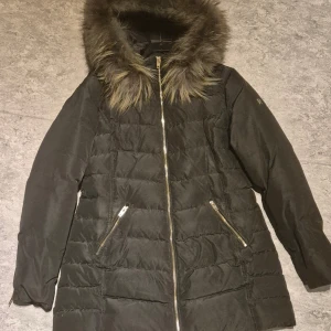 Svart dunjacka från Rockandblue - Snygg svart dunjacka från Rockandblue med pälskantad huva och dragkedja framtill. Jackan har långa ärmar och praktiska fickor med dragkedjor. Perfekt för kalla dagar!