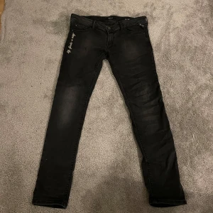 Svarta jeans från Replay - Snygga svarta jeans från Replay med broderad text 'Life finds a way' på sidan. De har  ett stretchigt material för extra komfort. Perfekta för en stilren look.