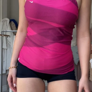 Rosa träningslinne från Nike - Säljer ett rosa träningslinne från Nike med en snygg racerback-design. Linnet har en tight passform och är perfekt för träning. Det har en liten vit Nike-logga på framsidan.