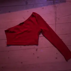 Snygg röd oneshoulder topp med lång ärm. Perfekt för en trendig look. Toppen är i en härlig röd färg och har en stilren design.
