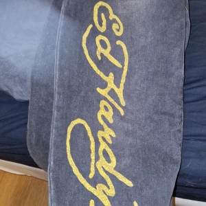 Gråa jeans från Ed Hardy - Coola svarta jeansbyxor från Ed Hardy med stort gult logotryck längs benet och en häftig vargdesign på benet. W30 och sitter löst och dint cider benen, samt går in lite i botten av venet så de inte släpar så mycket i marken😃