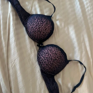 Svart och rosa leopardmönstrad push up bh  - Snygg bh med leopardmönster i svart och rosa. Den har justerbara axelband och en bekväm passform. Lappen avklippt men storlek är 75B. Använd fåtal gånger , Push up! Ena spännet är snett jämfört med det andra men går att knäppa utan några problem! 