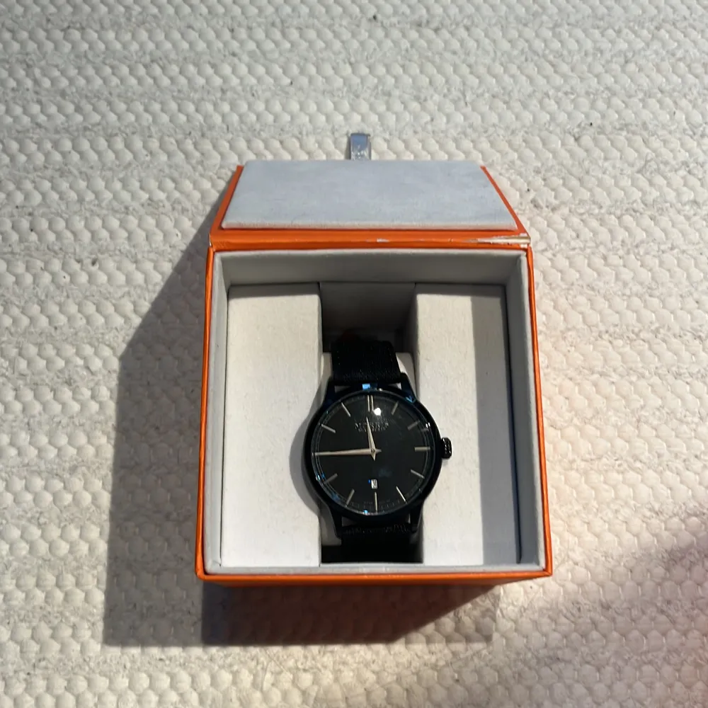 Elegant svart klocka från Morris med stilren design. Klockan har en svart urtavla med subtila markeringar och ett datumfönster. Armbandet är i svart material som ger en modern look. Perfekt för den som söker en tidlös accessoar.. Asusteet.