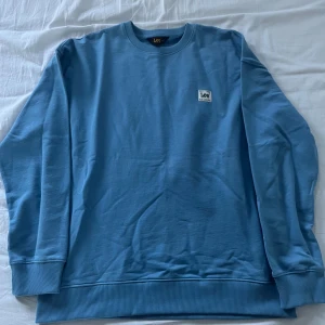 Blå sweatshirt från Lee - Säljer en snygg blå sweatshirt från Lee i loose fit. Tröjan har en rund halsringning och ribbade muddar vid ärmslut och nederkant. Perfekt för en avslappnad stil. Helt ny 