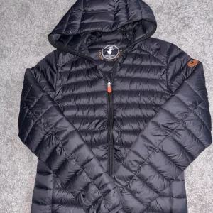 Svart pufferjacka från Save the Duck - Säljer en svart pufferjacka från Save the Duck i storlek S. Jackan är tillverkad med Plumtech syntetiskt dun och har en dragkedja framtill. Den är lätt och vattenavvisande med en huva för extra skydd. Perfekt för dig som vill ha en lätt jacka!