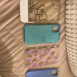 Mobilskal 11 iPhone  -  Olika mobilskalor för 11 iPhone en styck 30 kr,flera snygga mobilskal i olika stilar. Ett transparent skal med lila blommor, ett glittrigt turkost skal, ett blått skal och ett silverglittrigt skal. Perfekt för att ge din mobil en ny look!