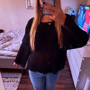 Svart blus med plisserade detaljer - Snygg svart blus med plisserade detaljer och långa ärmar. Blusen har en lös passform och är tillverkad i ett lätt och luftigt material. Nyskick!