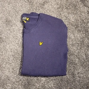 Mörkblå tröja från Lyle & Scott - Snygg mörkblå tröja från Lyle & Scott med v-ringning och deras ikoniska gula logga på bröstet.