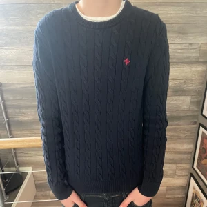 70% Rabatt - Stickad Morris Tröja  - Säljer en snygg mörkblå stickad tröja från Morris med kabelstickat mönster. Tröjan har en broderad röd logga på bröstet. Tröjan är i nyskick, utan ett enda märke, hål eller defekt. Den verkar vara ganska liten för sin storlek. Modell: ≈ 178 cm. Skick:10/10, Storlek: S/M, Nypris: ≈ 1699 kr. Vid eventuella frågor eller annat, hör av dig!