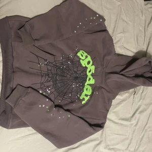Grå hoodie med spindelnätsmönster - Cool grå hoodie från Sp5der med ett iögonfallande spindelnätsmönster och gröna detaljer på bröstet. Hoodien har långa ärmar och är tillverkad i 100% bomull för en bekväm känsla. Perfekt för en avslappnad stil.
