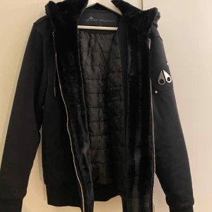 Moose knuckles classic bunny  - Säljer en svart jacka med huva från Moose Knuckles. Jackan har en quiltad insida och en snygg logotypdetalj på ärmen. Den är försedd med dragkedja och har en mjuk, pälsliknande kant på insidan av huvan. Original förpackning ingår inte.