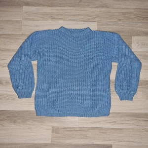 Blå hemmastickad tröja - Säljer en mysig blå hemmastickad tröja med ribbstickade muddar vid ärmslut och nederkant. Perfekt för kyliga dagar och ger en avslappnad look. Tröjan har långa ärmar och en rund halsringning.