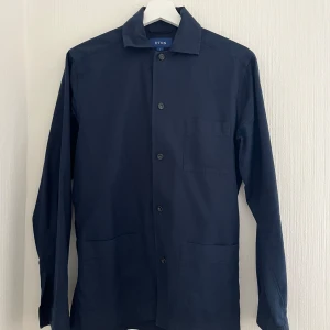 Mörkblå overshirt från Eton - Säljer en stilren mörkblå overshirt från Eton i 100% bomull. Den har en klassisk krage och knappar framtill. Perfekt för lager-på-lager-stil och passar till många olika outfits. XS men sitter mer som en S.