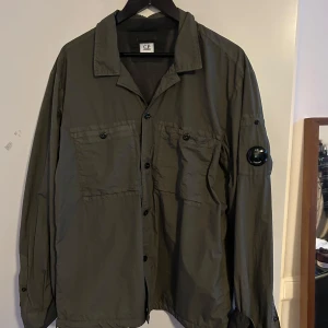 Grön overshirt från C.P. Company - Säljer en stilren grön overshirt från C.P. Company. Jackan har långa ärmar och knappar framtill. Den är perfekt för lager-på-lager och har en cool detalj på ärmen. Passar bra till både casual och mer uppklädda tillfällen.