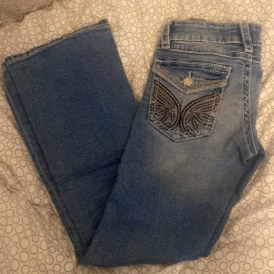 Blå jeans från Gina Tricot - Snygga blå jeans från Gina Tricot med dekorativa broderier på bakfickorna. De har en klassisk femficksdesign och knappgylf. Perfekta för en avslappnad stil.