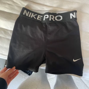 Svarta träningsshorts från Nike pro - Säljer ett par svarta Nike Pro träningsshorts i storlek S. De har en elastisk midja med Nike-logga och är perfekta för träning. Shortsen är tillverkade i ett stretchigt material för optimal rörelsefrihet.