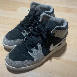 Nike Air Jordans i svart och grått - Snygga Nike Air Jordans i svart och grått med vit sula och klassisk snörning. Skorna har ett unikt mönster på gråa partier och en vit Nike-logga på sidan. Perfekta för en stilren look.