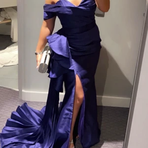 Festklänning  - Elegant mörkblå långklänning med offshoulder-design och en djärv slits framtill. Använd endast ett fåtal timmar. Perfekt till bal eller bröllop.  Nypris 3500kr 