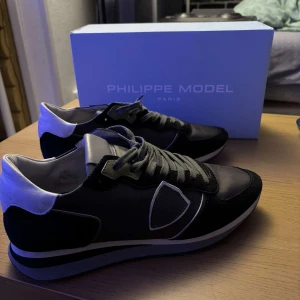 Svarta sneakers från Philippe Model - Snygga svarta sneakers från Philippe Model med vita detaljer och snörning. Skorna har en stilren design med en diskret logga på sidan. Perfekta för en casual look.