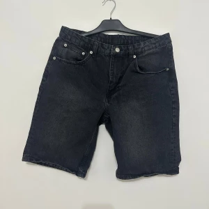 Svarta jeansshorts - Snygga svarta jeansshorts med klassisk femficksdesign och knappgylf. Perfekta för en avslappnad stil. De har en normal passform och kan enkelt rullas upp för en mer casual look.